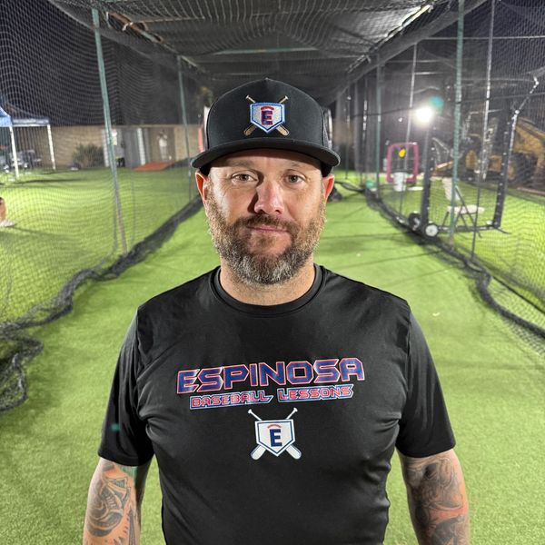 Man in baseball gear standing in a batting cage at night.