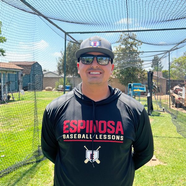 Man wearing Espinosa Baseball Lessons hoodie and cap, standing in a batting cage.