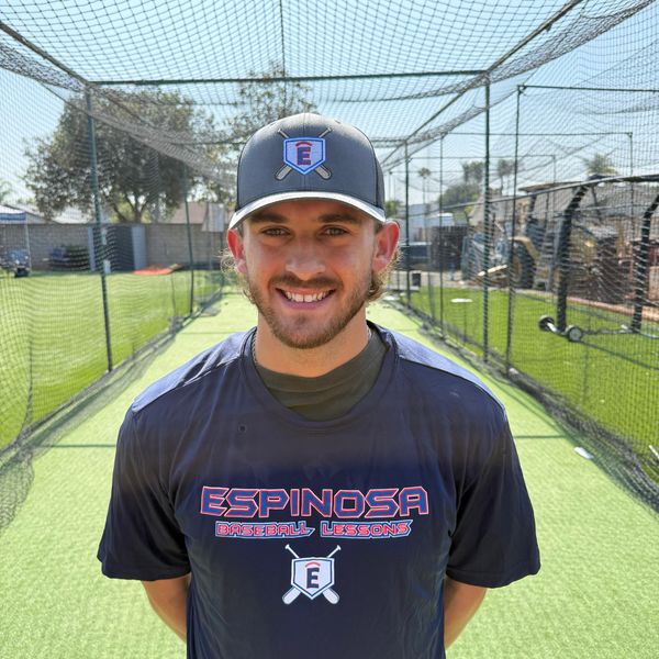 Smiling baseball coach in a batting cage wearing Espinosa Baseball Lessons shirt.