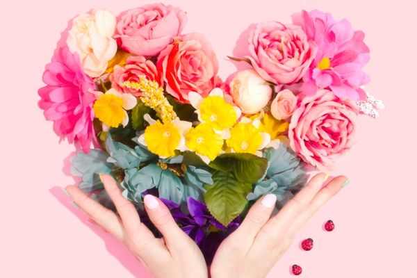 Hands holding a colorful bouquet of flowers against a pink background.