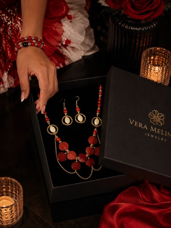 Hand holding a box with red and gold jewelry set.