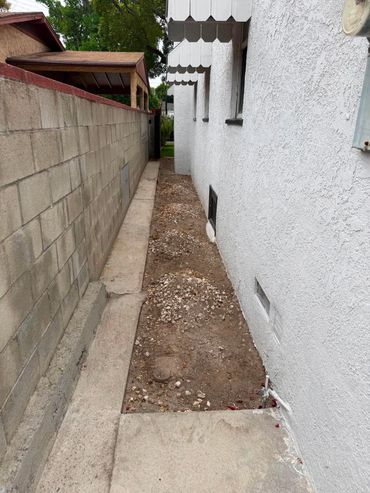 Narrow pathway with gravel next to a white house and brick wall.