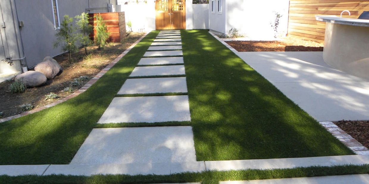 Modern backyard pathway with alternating stone slabs and green grass.