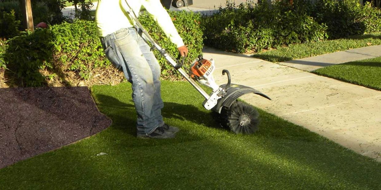 Person using a power broom to clean artificial grass outdoors.