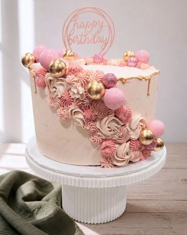Elegant pink and gold birthday cake with decorative frosting and spheres.