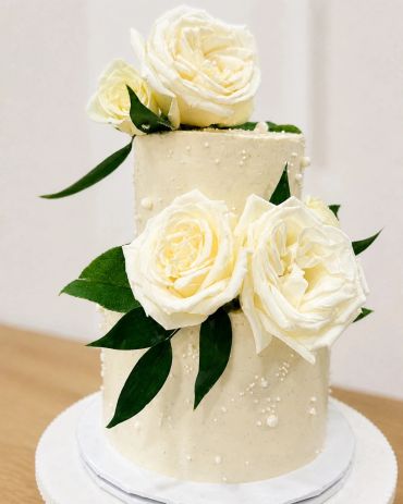 Elegant white cake with white roses and green leaves.