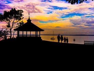 Silhouetted family by a lakeside pavilion during vibrant sunset.
