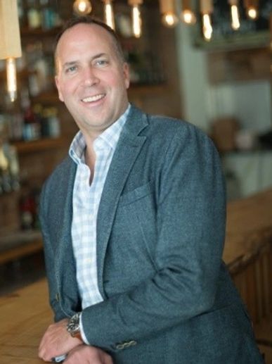 Man in a gray blazer smiling at a bar or restaurant counter.