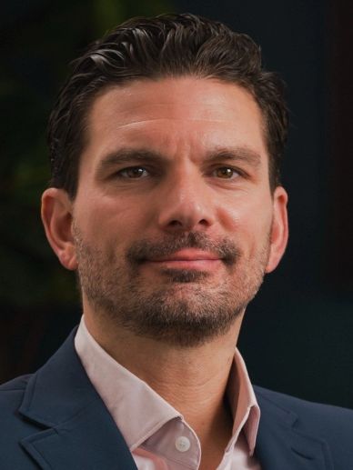 Confident man with short dark hair and beard in a suit jacket.