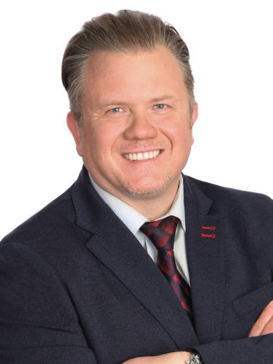Smiling man in a suit with crossed arms against a white background.