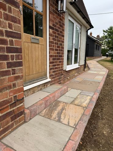 A newly paved stone pathway alongside a brick house with a wooden door.