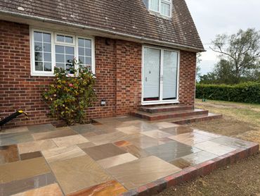 Newly paved patio outside a brick house with wet stone tiles.