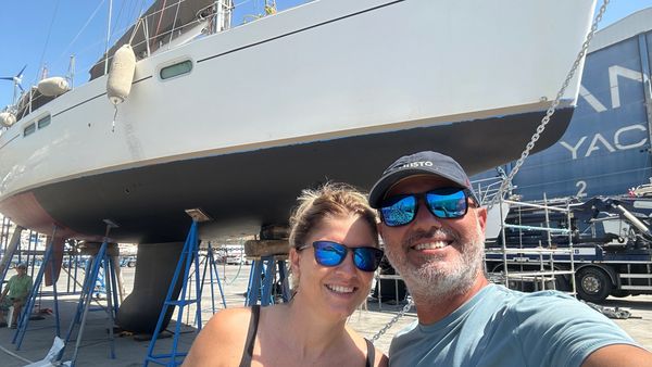 A happy couple takes a selfie in front of a large boat on dry dock.