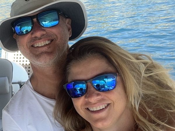 Smiling couple wearing blue reflective sunglasses on a boat with water in the background.