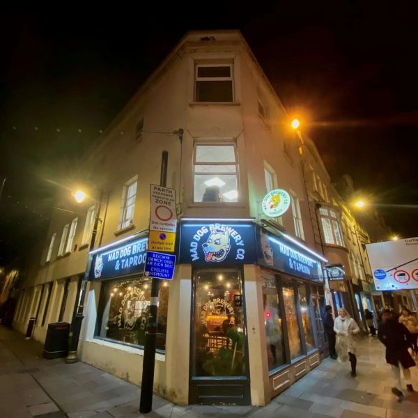 Night view of Mad Dog Brewery & Taproom on a street corner.