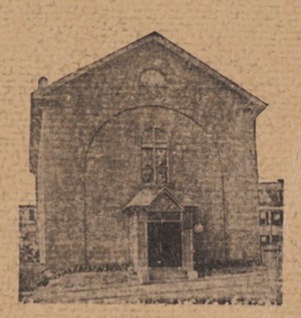Old photograph of a stone building with an arched entrance.
