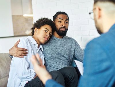 Man with his arm around his son as they are listening to a man provide therapy 