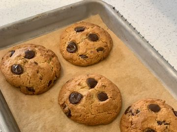 Freshly baked chocolate chip cookies on a baking tray lined with parchment paper.