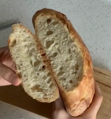 A person holding a freshly baked loaf of bread cut in half.