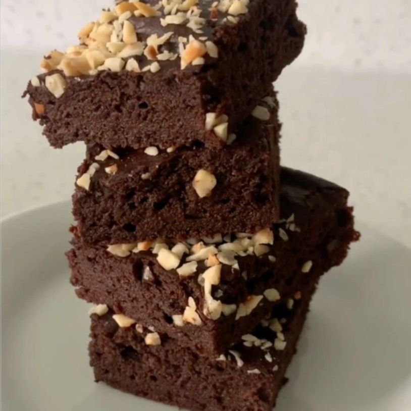 Stack of chocolate brownies topped with chopped nuts on a white plate.