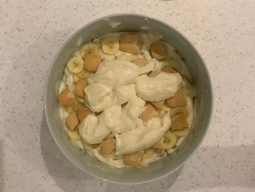 A bowl of banana slices, vanilla wafers, and whipped cream.