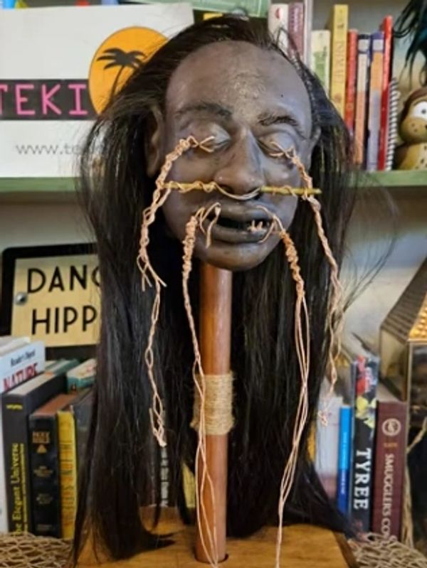 A carved head with long hair and string decorations on a wooden stand.