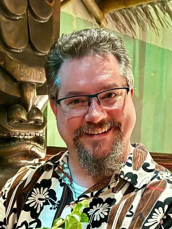 Smiling man with glasses in a floral shirt.