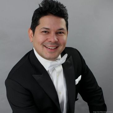 Smiling man in a black tuxedo with a white bow tie against a gray background.