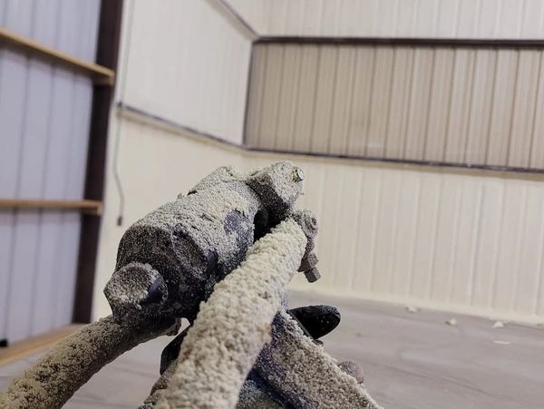 Close-up of a spray gun covered in a thick layer of dried foam or paint in an industrial setting.