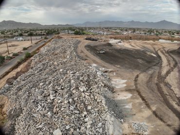 Aerial drone view of a Phoenix material site showing debris piles, retention pond, and active earthw