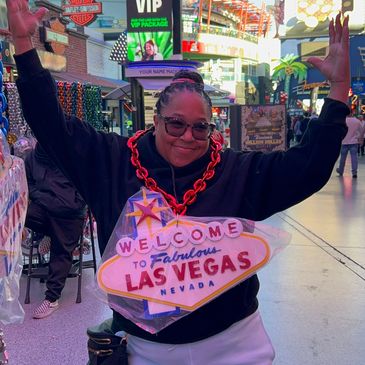 Person joyfully posing with a large "Welcome to Fabulous Las Vegas" sign necklace on a busy street.