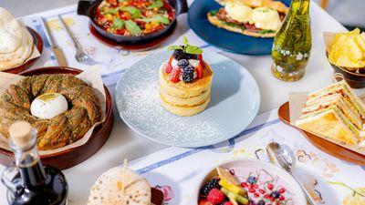 A vibrant brunch spread featuring pancakes, bagels, sandwiches, and fresh fruit.