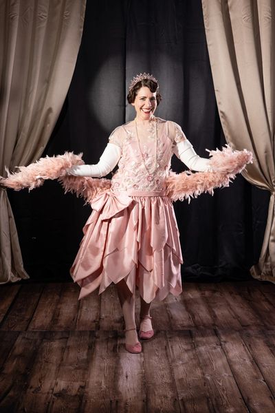 Woman in 1920s dress of pink taffeta with feather boa. Dressed like Cora Crawley from Downton Abbey.