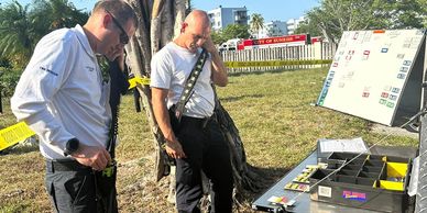 Two men using a communication device outdoors beside a table with equipment.