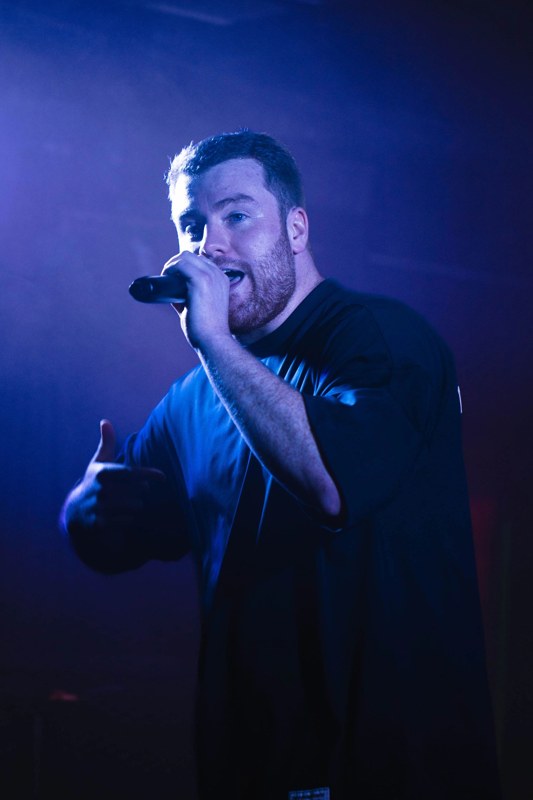 Man passionately singing into microphone under blue stage lighting.