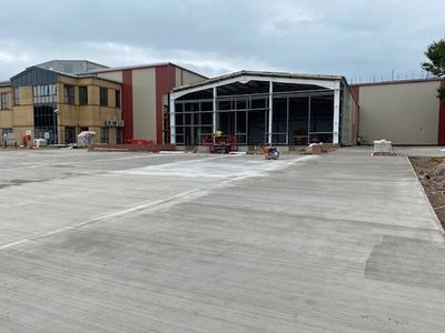 Construction site with newly poured concrete in front of industrial buildings.