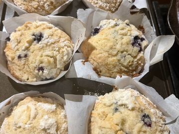 Freshly baked blueberry muffins with crumbly topping in paper liners.
