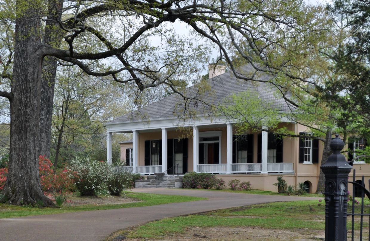 Historic Southern-style house with large porch and surrounding greenery.