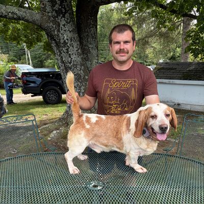 Man posing with a white and brown dog on a metal table outdoors.