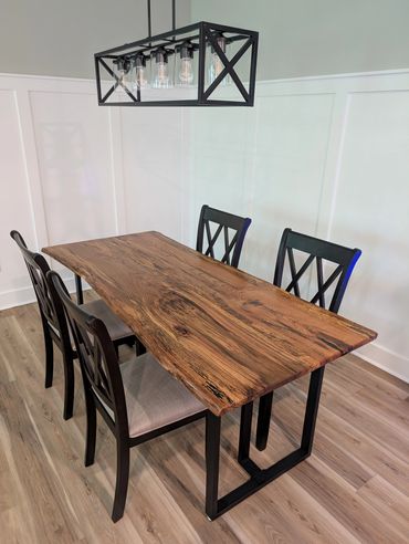 Modern dining table with natural wood top and black chairs under a geometric chandelier.