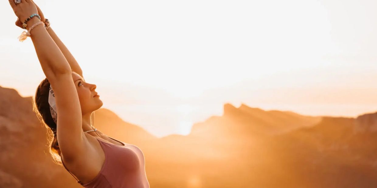 Woman practicing yoga with arms raised during a golden sunset in the mountains.