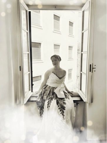 Woman in vintage dress sitting by an open window, softly lit.