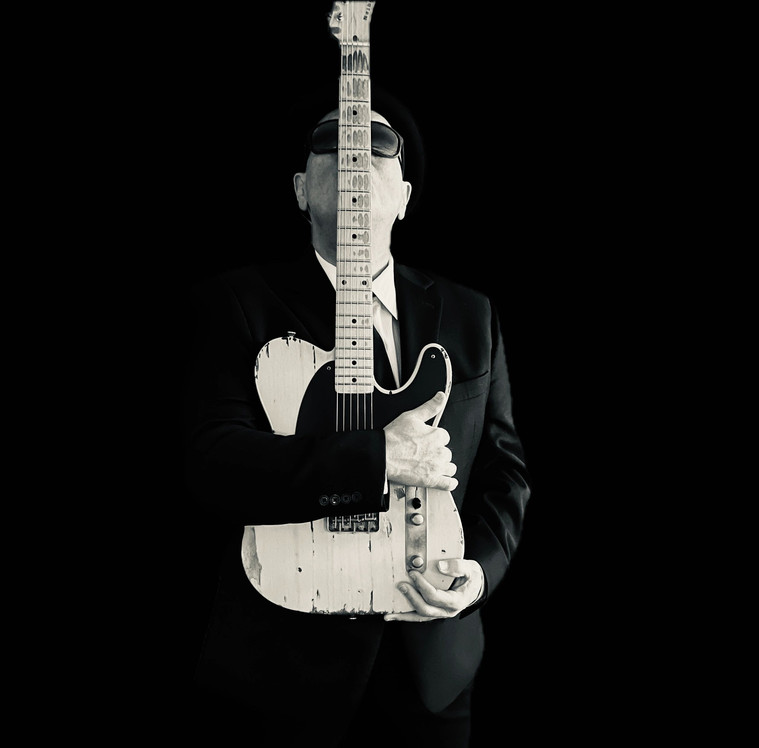 Man with a guitar covering his face in black and white.