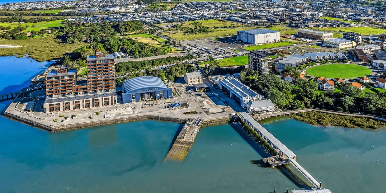 Aerial view of a coastal town with docks, buildings, and green spaces under a blue sky.