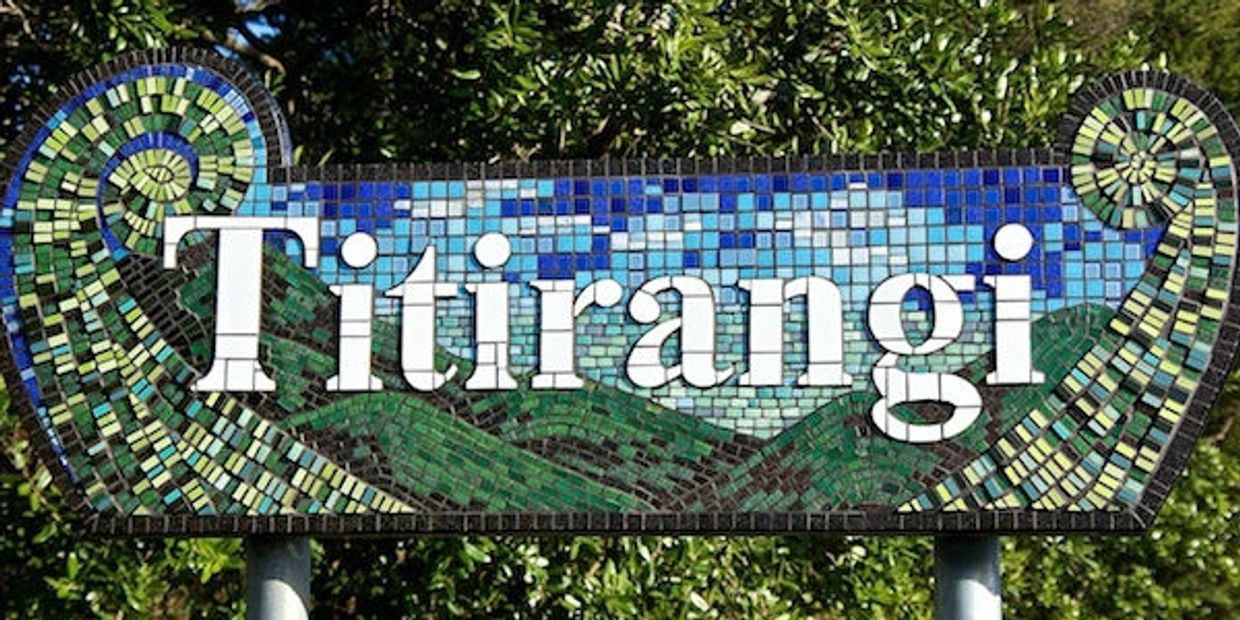 Colorful mosaic sign reading 'Titirangi' with green hills and sky background.