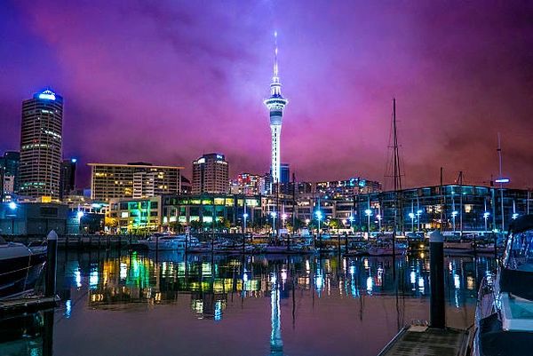 Night view of a city skyline with a tall illuminated tower and marina reflections.