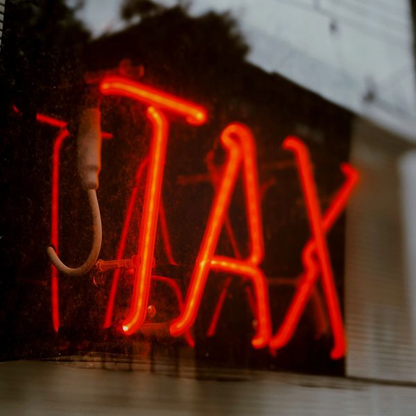 Red neon sign displaying the word 'TAX' glowing in the dark.