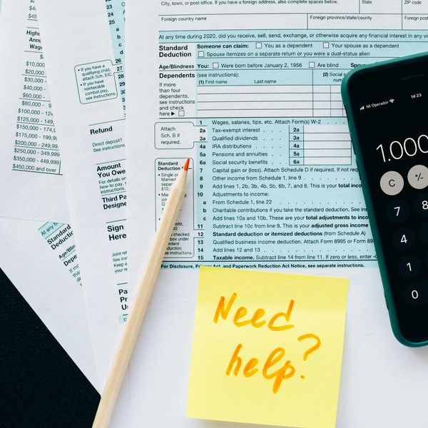 Tax forms with a pencil, calculator, and sticky note saying 'Need help?'.