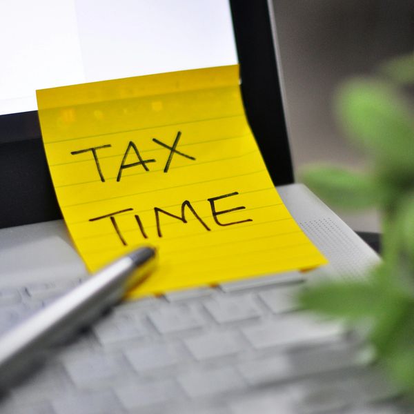 Yellow sticky note with 'TAX TIME' on a laptop keyboard with a pen nearby.