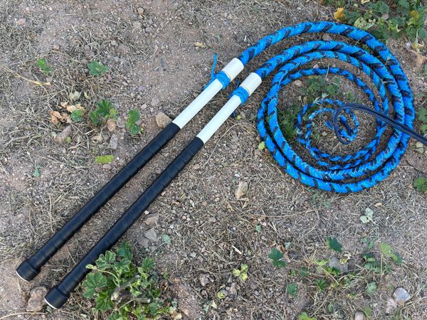 A blue whip with a white handle lying on grass.